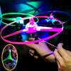 A hand holds a glowing pink UFO spinning top with a pull string, demonstrating the LED flying disc toy.