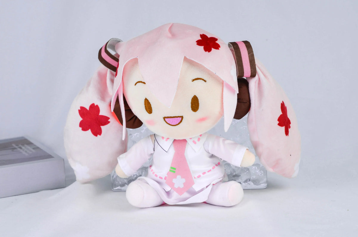 A pink Hatsune Miku plush doll with large ears and a white outfit, featuring red flower accents.