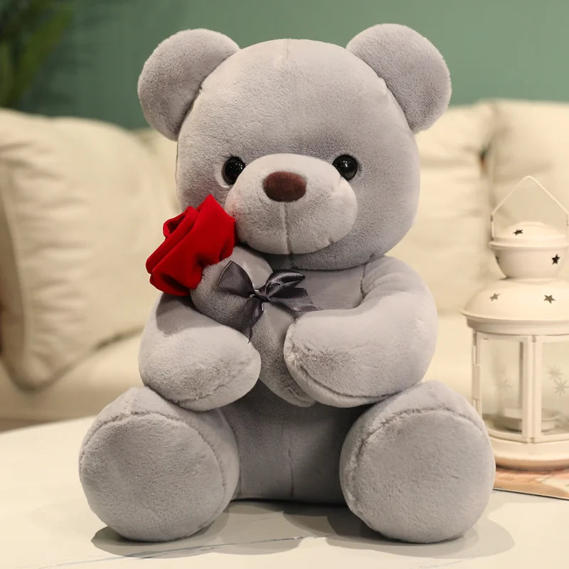 A gray teddy bear plush toy holding a red rose, sitting on a white surface.