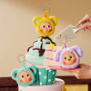 A hand holds a tiered cake decorated with plush animal figures, including a yellow bear and a purple creature.
