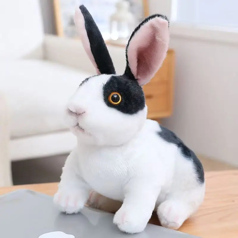 A white rabbit plush toy with black markings and pink ears sitting on a wooden surface.
