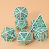 A set of seven polyhedral dice in white and green patterns arranged on a light brown surface.