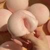 A hand holds a pink mochi squishy toy, showing its soft texture and round shape against other similar toys.