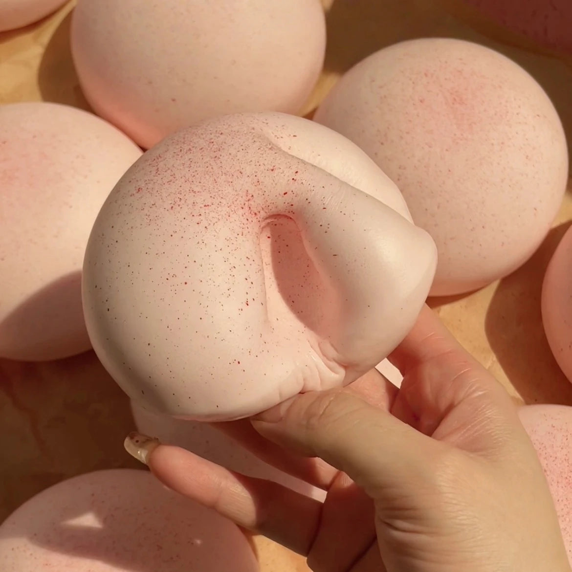 A hand holds a pink mochi squishy toy, showing its soft texture and round shape against other similar toys.