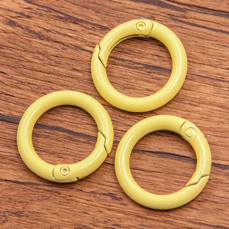 A set of ten yellow metal O-ring spring clasps arranged on a wooden surface.