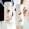 A white reusable water bottle with dog stickers featuring cartoon dogs, held by a person.