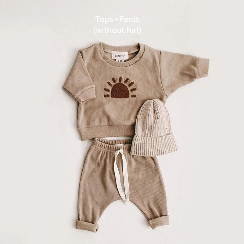 A beige baby girl outfit set featuring a long-sleeve top and matching pants with a knit hat.