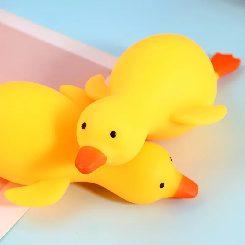 A bright yellow squishy duck fidget toy is shown lying on a light blue surface.