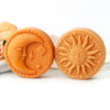Two round orange silicone molds shaped like the sun and moon for candles and soap making