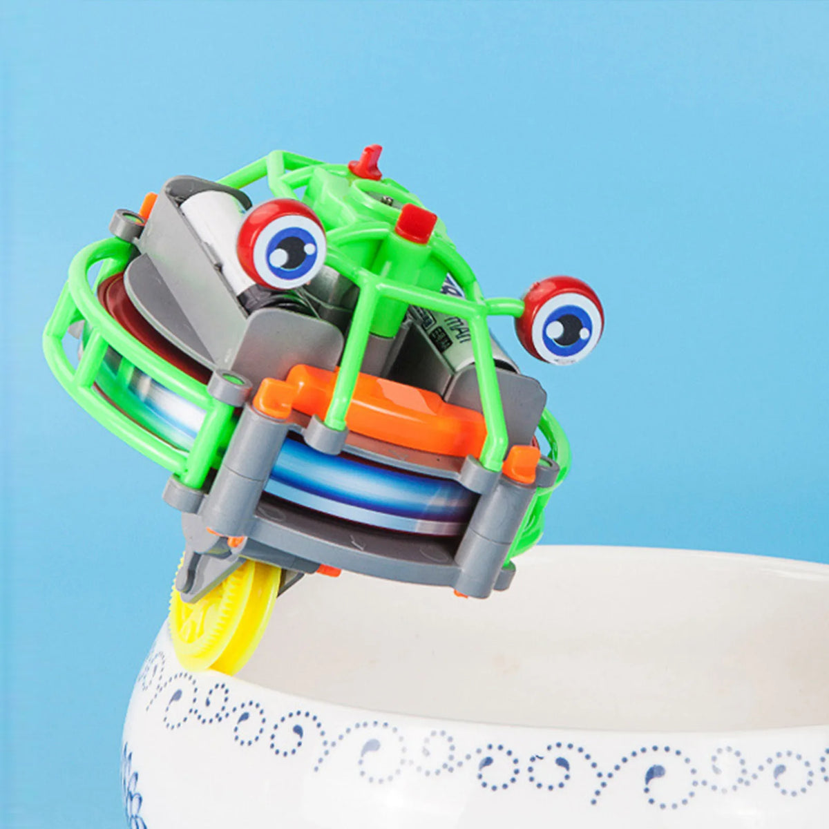 A green and gray gyroscopic unicycle fingertip spinner toy with large eyes is shown on a white surface.