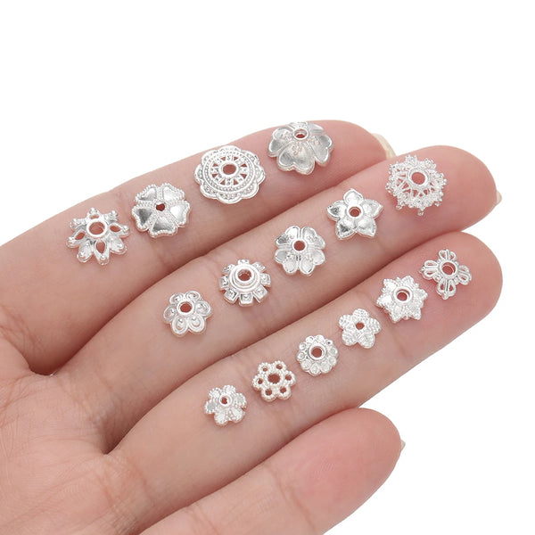A collection of silver alloy flower shape bead caps for jewelry making displayed on a hand.