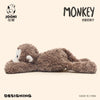 A fluffy brown monkey plush toy is shown lying down on a light background.