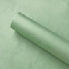 A roll of translucent tissue paper sheets lying on a light green surface.