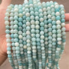 A hand holds a strand of natural Amazonite beads for jewelry making, featuring light blue and white tones.