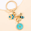 Gold-toned keychain featuring a honeycomb and bee charm with blue enamel and a daisy flower.