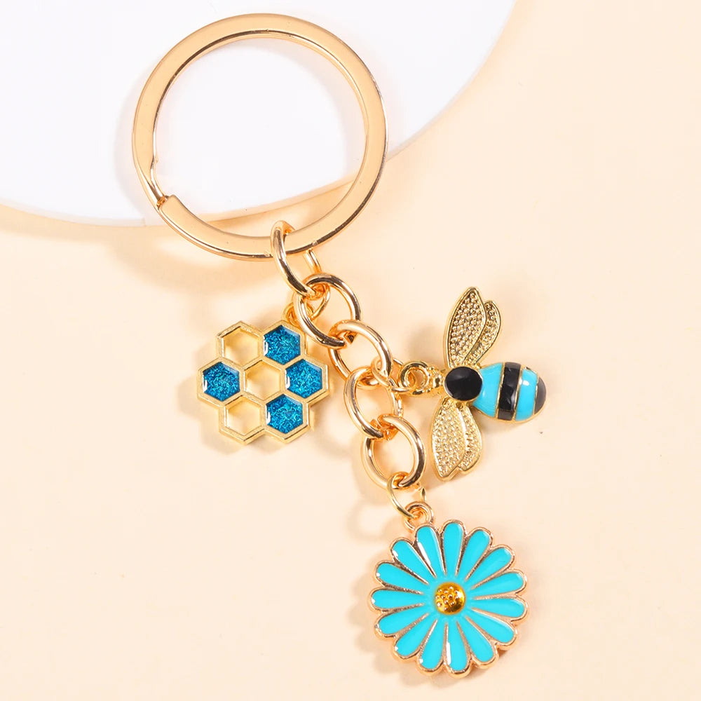 Gold-toned keychain featuring a honeycomb and bee charm with blue enamel and a daisy flower.