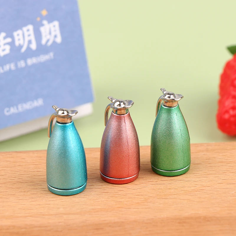 Three miniature alloy kettles in teal, copper, and olive green sitting on a wooden surface.