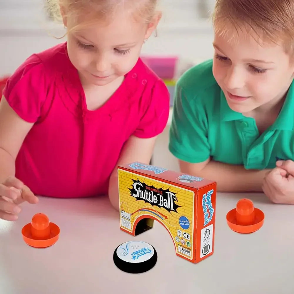 Two children look at a box of the Shuttle Ball mini floating air hockey set with two pushers on a table.