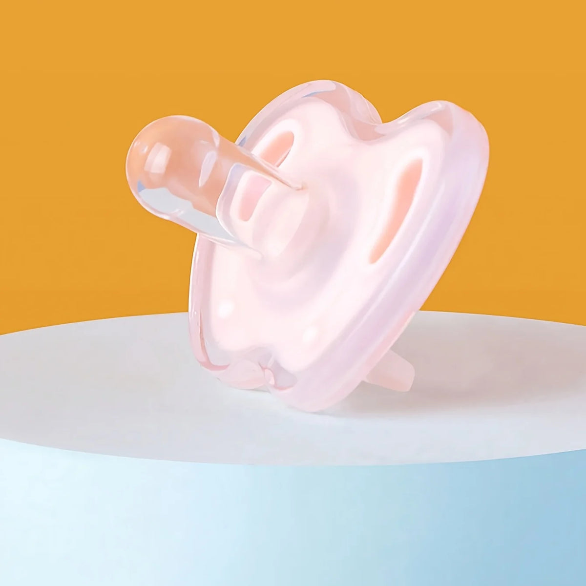 A pink silicone baby pacifier is shown against an orange background on a white surface.