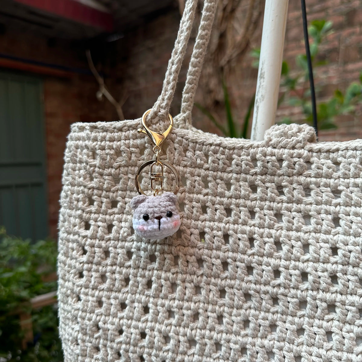 A light beige crocheted bag with a gold-toned animal keychain attached to the strap.