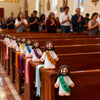 A set of small white religious statues depicting Jesus with a heart, placed on wooden church pews.