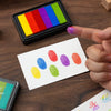 A hand holds a rectangular ink pad set featuring six large, brightly colored gradient pads for crafting and stamping.
