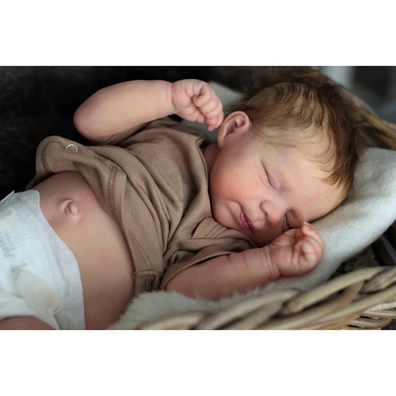 A newborn baby doll with rooted hair sleeping peacefully, wrapped in a brown garment.