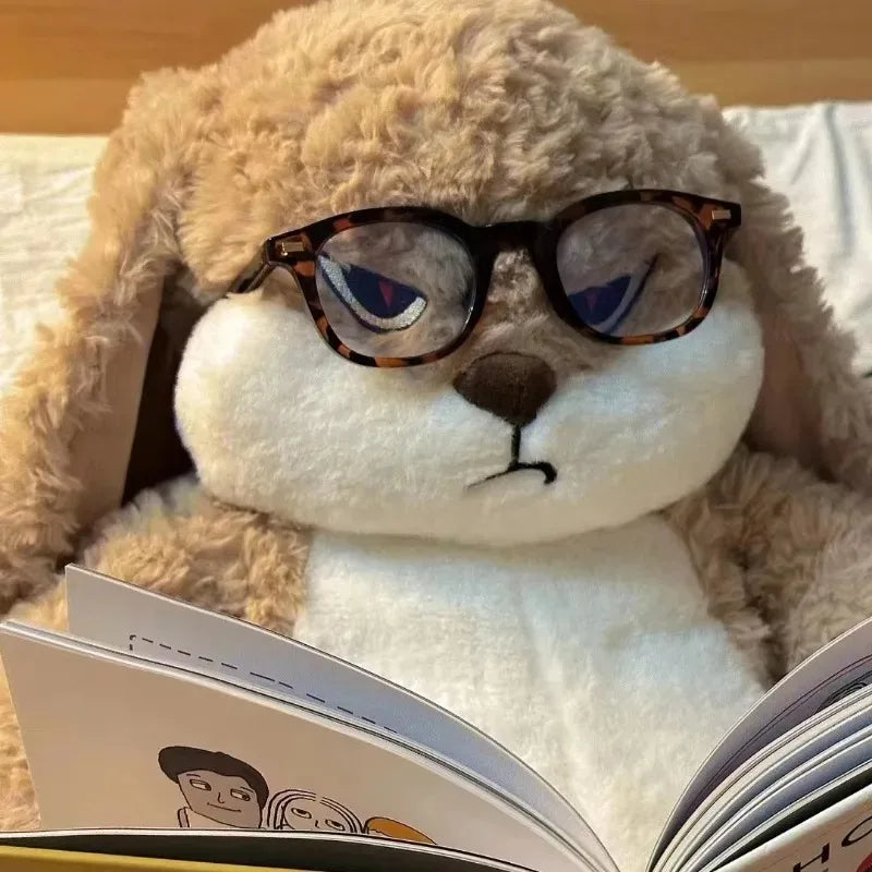 Un ours en peluche lapin fâché portant des lunettes regarde un livre ouvert.