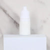 A white bottle with a white dropper cap sits on a white surface.