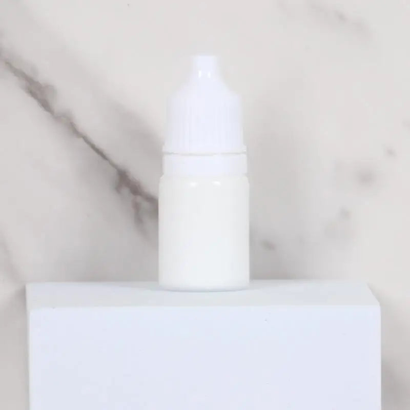 A white bottle with a white dropper cap sits on a white surface.