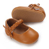 A pair of tan leather moccasin shoes for a baby girl with a braided lace trim and bow.