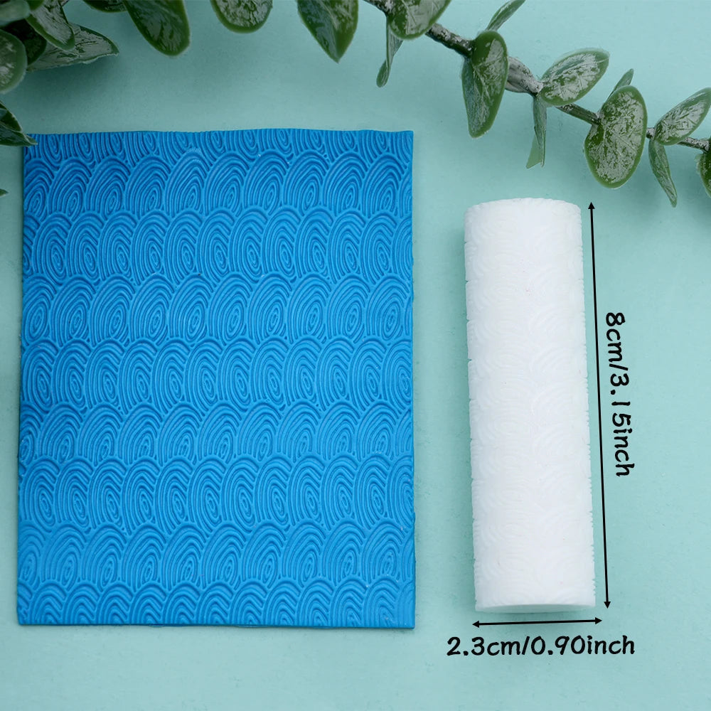A roll of white clay texture rollers next to a blue patterned surface and green leaves.