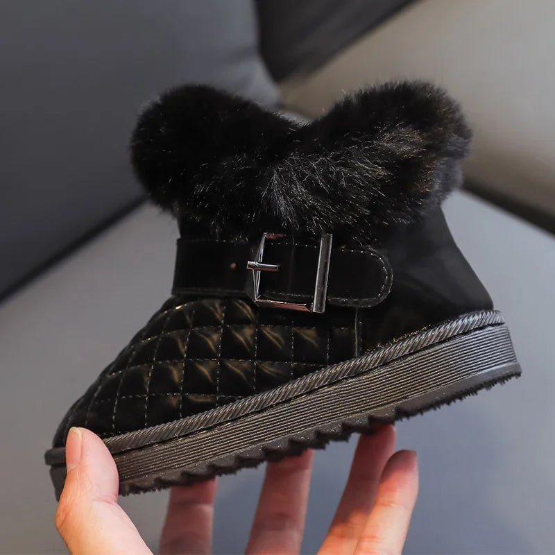 A close-up of black crystal bowknot snow boots with a black faux fur lining and a silver buckle being held by a hand.