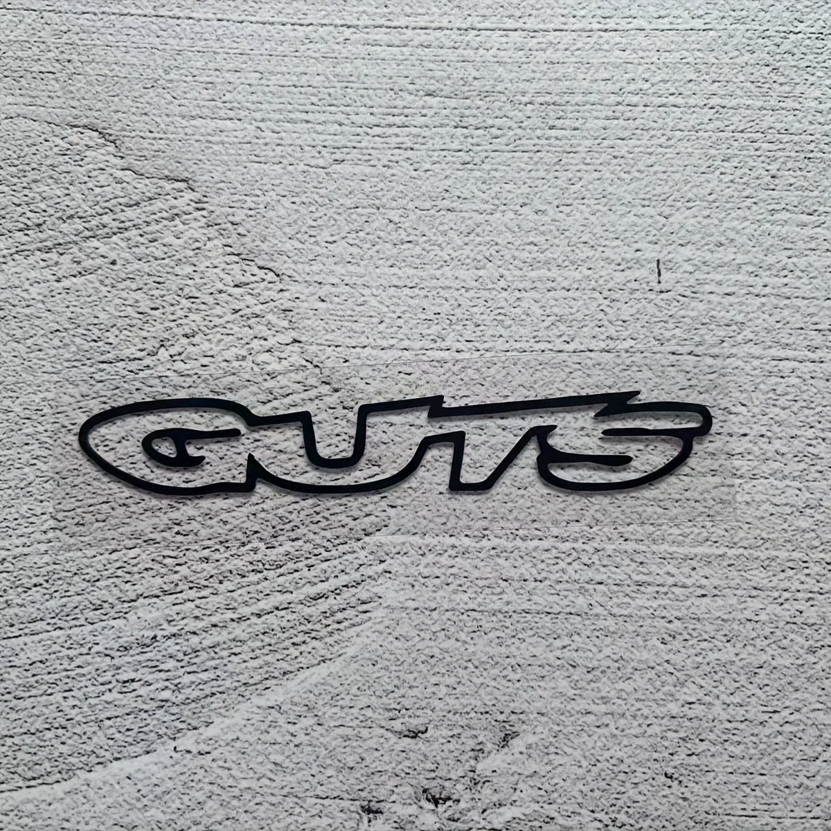 A black vinyl sticker with the word GUTS is placed on a textured gray surface.