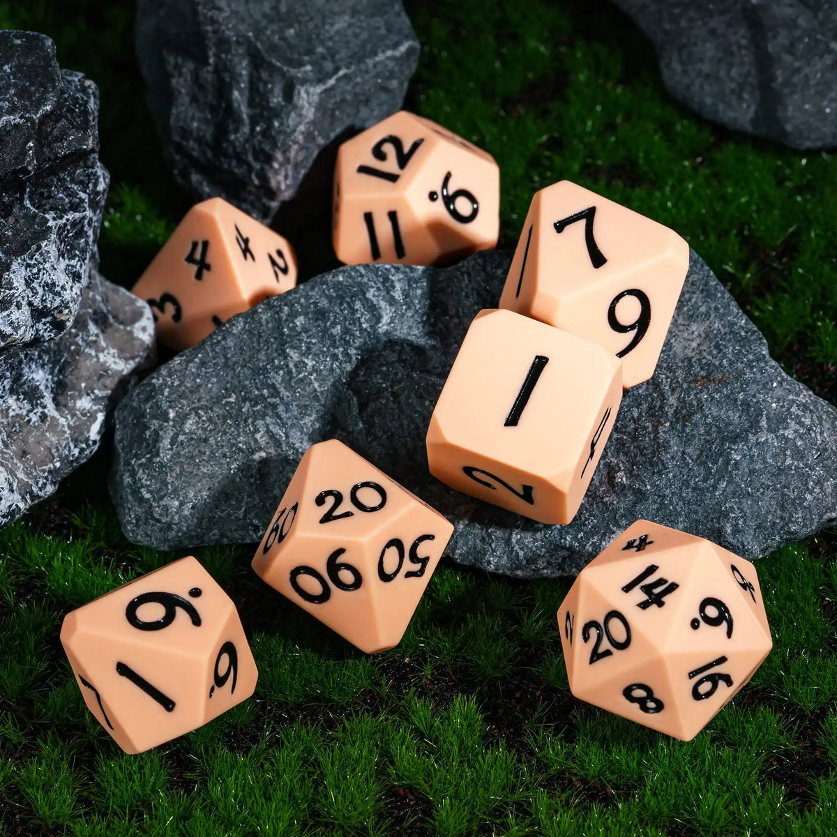 A set of orange silicone polyhedral dice resting on green grass next to dark rocks.