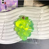 A translucent green squishy grape fidget toy is visible inside a clear plastic pouch, resting on a white silicone mat.