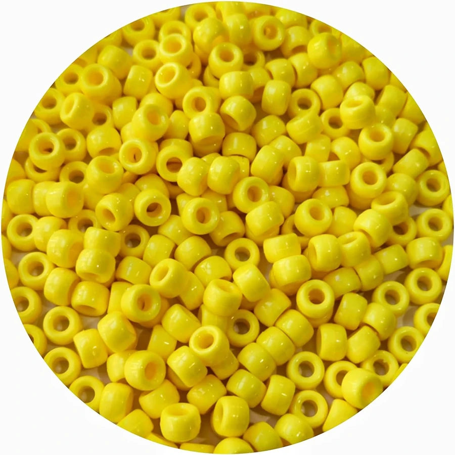 A close-up view of small yellow pony beads scattered on a white background.