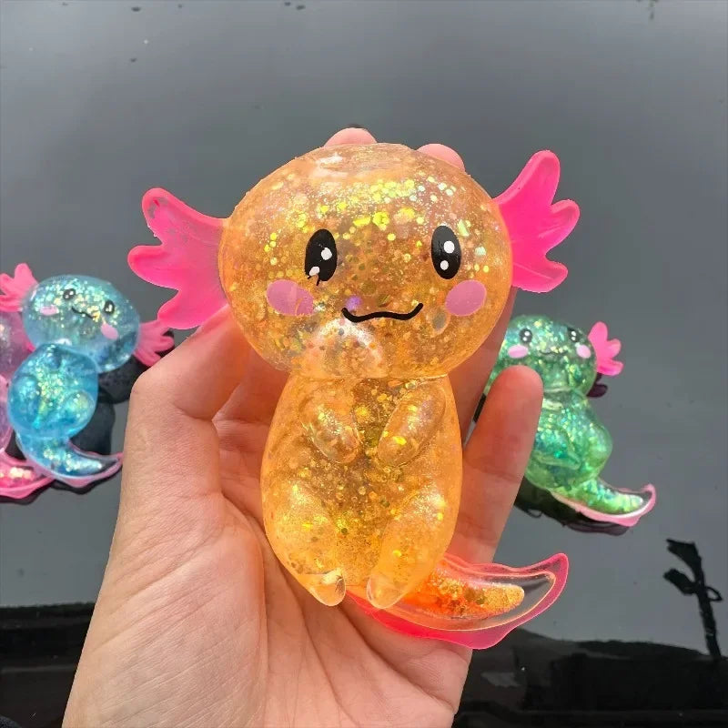 A hand holds a squishy axolotl stress relief toy with bright orange and pink translucent body and fins.