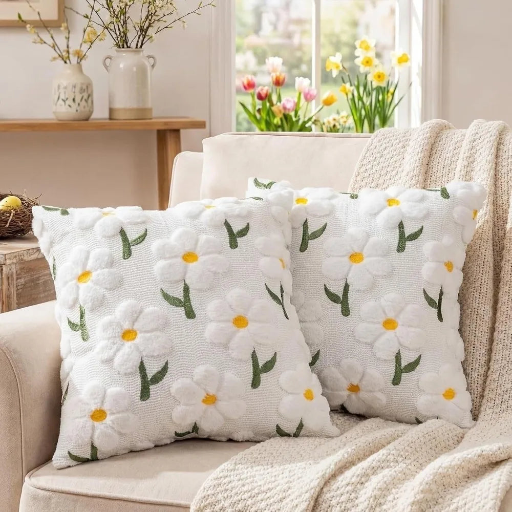 White faux fur pillow covers with embroidered yellow daisy designs resting on a beige sofa.