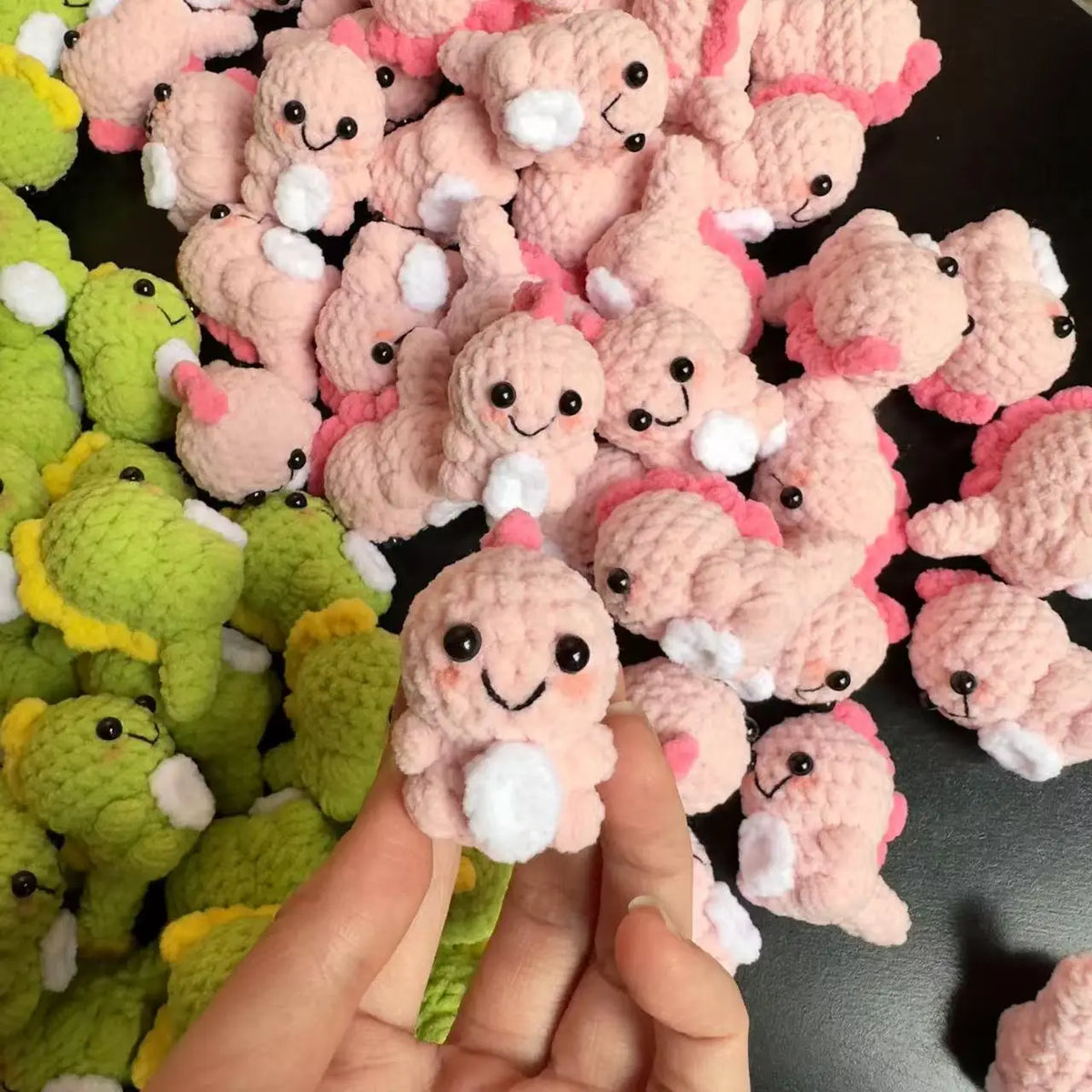 A close-up of many handmade crochet dinosaur keychains in pink and green colors.
