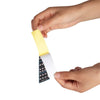 A hand is peeling a yellow note sticker from a black and white sheet for violin fretboard practice.