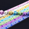 A close-up of colorful glitter origami star paper strips arranged diagonally on a dark background.