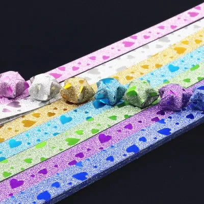A close-up of colorful glitter origami star paper strips arranged diagonally on a dark background.