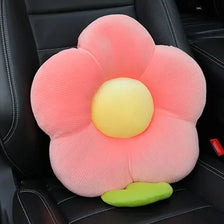 A pink plush lumbar support pillow with a yellow center and green base resting on a black car seat.