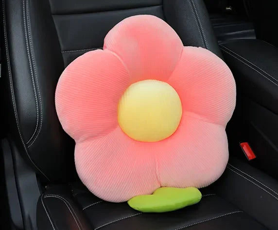 A pink plush lumbar support pillow with a yellow center and green base resting on a black car seat.