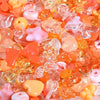 A close-up view of mixed loose acrylic beads in shades of orange, pink, and yellow for jewelry making