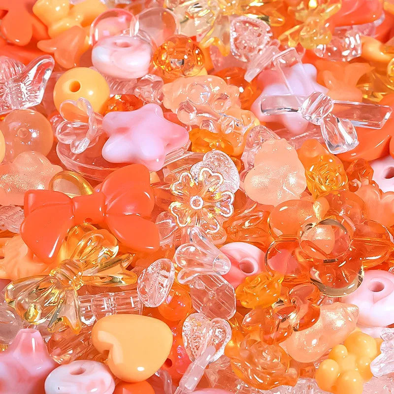 A close-up view of mixed loose acrylic beads in shades of orange, pink, and yellow for jewelry making