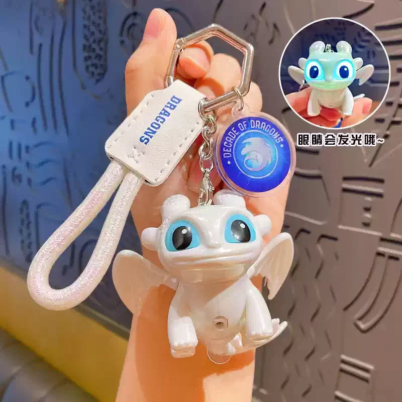 A white Toothless Dragon keychain featuring movable wings and glowing blue eyes, held by a person.