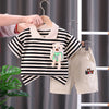 A striped kids outfit set featuring a black and white shirt and beige shorts hanging on a wooden hanger.