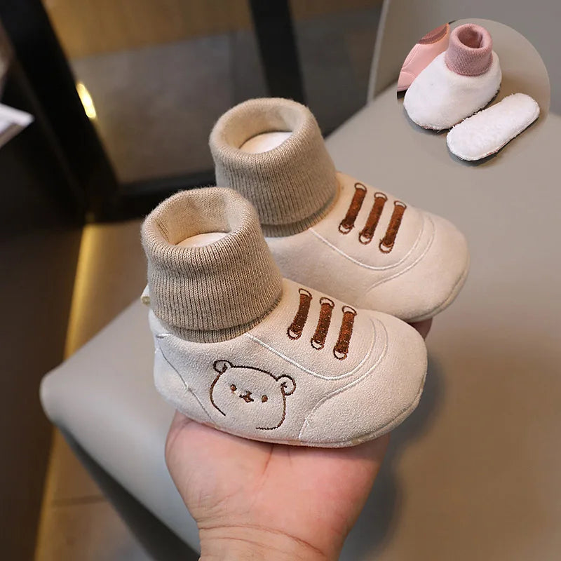 A pair of beige knit bear booties for a baby, shown next to other soft knitted items.